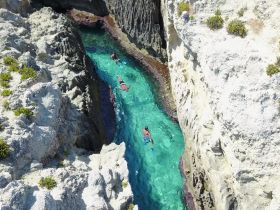 Snorkelers explore the stunning turquoise waters surrounded by dramatic rock formations, capturing the essence of adventure in a picturesque natural setting.