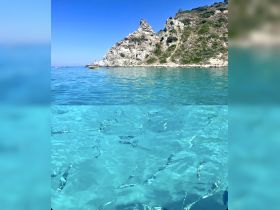 A stunning view of crystal-clear waters revealing underwater life, framed by a picturesque rocky coastline — perfect for snorkeling and exploring marine beauty.