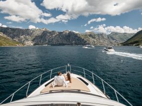 A couple enjoys a scenic view from the bow of a yacht, surrounded by stunning mountains and clear waters — a perfect moment for romantic getaways or celebrations.