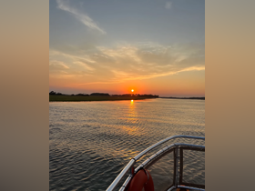 A serene sunset view from the bow of a boat, reflecting golden hues on the water — a perfect backdrop for evening cruises.