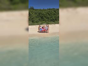 A cheerful group poses on the beach with a flag, capturing a memorable moment during their tropical getaway — perfect for celebrations and group trips.