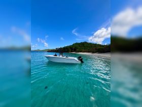 A boat anchored in crystal-clear turquoise waters near a sandy beach, with a person onboard enjoying the serene island setting.