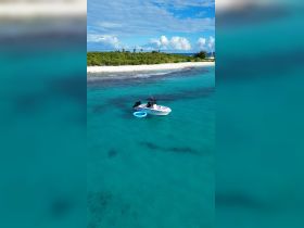 Aerial view of a sleek boat anchored in crystal-clear turquoise waters, surrounded by a picturesque beach and lush greenery — ideal for exploring tropical destinations.