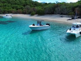Aerial view of two boats anchored in crystal-clear waters near a sandy beach, showcasing a serene tropical getaway perfect for boating enthusiasts.