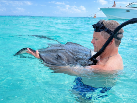 A man interacts with a stingray in crystal-clear waters, showcasing a unique wildlife experience that highlights the beauty of marine life.