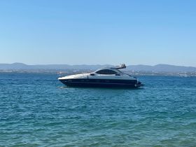 A sleek yacht glides through clear waters, showcasing its elegant design against a scenic backdrop of distant hills.