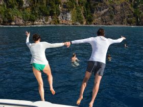 A couple joyfully jumps into the clear blue waters, capturing the thrill of adventure and fun during their boating experience.