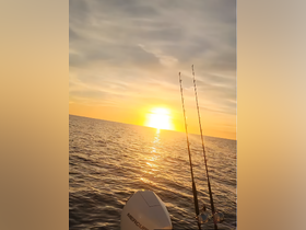 A serene sunset view over the ocean with fishing rods in the foreground, capturing the essence of a peaceful fishing experience on the water.