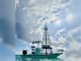 A stunning view of a boat near a lighthouse, showcasing the vibrant colors of the vessel against a backdrop of dramatic skies — perfect for exploring coastal waters.