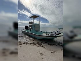 A fishing boat rests on the sandy shore, showcasing its sleek design against a backdrop of cloudy skies — perfect for a day of adventure on the water.
