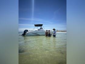 A family enjoys a sunny day in shallow waters next to their boat, creating lasting memories of fun and adventure at the beach.