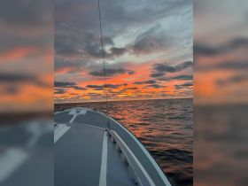 A stunning sunset view from the bow of a boat, showcasing vibrant colors reflecting on the ocean — perfect for serene evening cruises.
