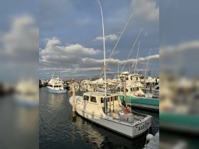 A serene view of the fishing boat 'Kaitlyn' docked in the marina, surrounded by other vessels under a cloudy sky.