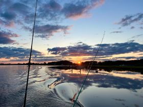 A serene sunset view over calm waters, with fishing rods in the foreground, capturing the tranquility of a perfect evening on the water.