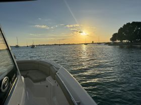 A serene sunset view from the deck of a boat, showcasing the tranquil waters and distant vessels — perfect for evening cruises.