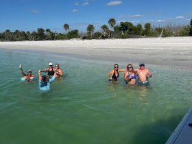 A lively group enjoys a beach day, celebrating with drinks in the shallow water — perfect for fun and relaxation under the sun.