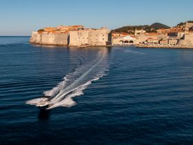 A stunning aerial view of a boat cruising near the historic coastline of Dubrovnik, showcasing the beautiful architecture and clear waters — perfect for exploring this iconic destination.