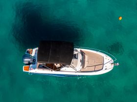 Aerial view of a sleek boat anchored in crystal-clear waters, showcasing its elegant design and inviting deck space.