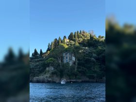 A picturesque view of a boat anchored near a stunning coastal hillside, showcasing beautiful architecture and lush greenery — a perfect representation of serene boating experiences.