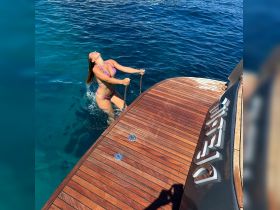 A woman joyfully climbs the ladder of a boat after a refreshing swim in crystal-clear waters, capturing the essence of summer fun and adventure on the water.