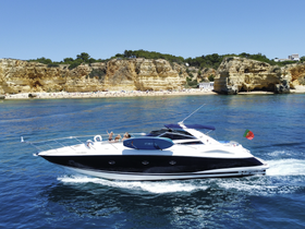 A lively group enjoys a sunny day aboard a sleek boat, cruising near a beautiful beach with golden cliffs — perfect for summer adventures and celebrations on the water.