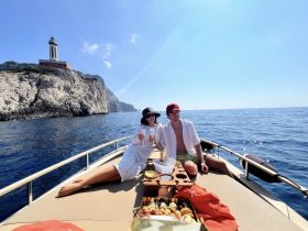 A couple enjoys cocktails on a boat with a stunning lighthouse backdrop, perfect for romantic getaways and scenic cruises.