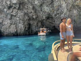 A couple poses on the deck of a boat near a stunning cave, surrounded by crystal-clear waters — a perfect moment capturing the beauty of their adventure.