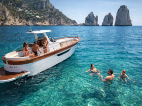 A lively group enjoys a sunny day on the water, with some swimming and others relaxing on the boat, showcasing the perfect summer getaway.