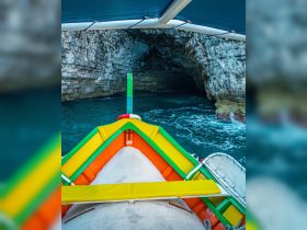 A vibrant view from the front of a boat approaching a stunning cave, showcasing the beautiful turquoise waters and rocky cliffs.