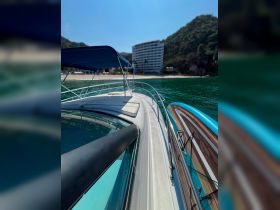 A sleek view of a yacht's exterior, showcasing its elegant design against a backdrop of clear waters and a beach resort, perfect for luxury boating experiences.