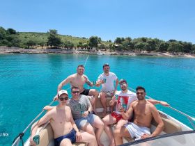 A group of friends enjoys a sunny day on a pontoon boat, raising their drinks in celebration against a backdrop of stunning turquoise waters and a scenic beach.