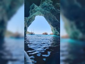 A stunning view from inside a cave, showcasing boats anchored outside and people swimming in the crystal-clear waters — a perfect spot for island hopping adventures.