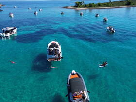A vibrant scene of people enjoying the clear turquoise waters, with boats anchored nearby and swimmers in the foreground, perfect for a fun day on the water.