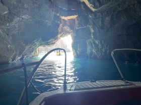A stunning view from inside a cave, showcasing the vibrant blue waters and a boat exiting the cave, with people visible enjoying the experience — a perfect adventure for exploring coastal wonders.