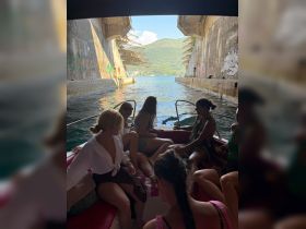 A lively group of friends enjoys a boat ride through a scenic passage, surrounded by stunning landscapes and vibrant graffiti — perfect for memorable summer adventures.