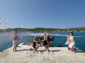 A joyful marriage proposal unfolds on a picturesque pier, surrounded by friends celebrating with champagne and rose petals — a perfect moment for unforgettable memories.