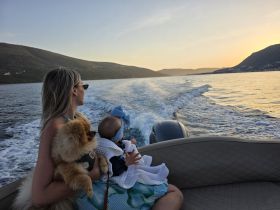A woman enjoys a sunset boat ride with her baby and dog, capturing a serene family moment on the water.