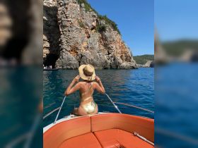 A woman enjoys the stunning coastal scenery while relaxing on the bow of a boat, perfect for sunbathing and exploring beautiful destinations.