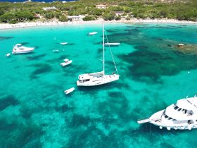 Aerial view of a catamaran and several smaller boats anchored in crystal-clear turquoise waters, showcasing a serene coastal landscape perfect for boating adventures.