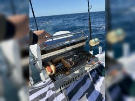 A close-up of a Magma grill on a boat, featuring hot dogs ready for grilling — perfect for enjoying meals on the water.