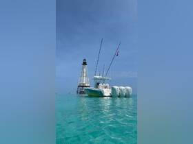 A sleek speedboat named 'Big Guru' is anchored near a lighthouse, showcasing the vibrant turquoise waters — perfect for fishing or leisure outings.