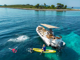 A fun day on the water with guests swimming and paddleboarding near a stylish boat in crystal-clear waters, perfect for summer adventures.