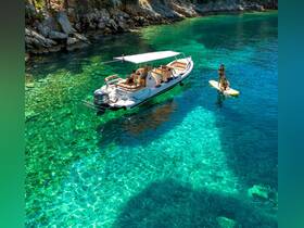 A group enjoys paddleboarding in crystal-clear waters beside a stylish boat, showcasing the perfect summer day on the water.