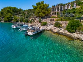 A stunning aerial view of several boats docked along a rocky shoreline, surrounded by crystal-clear waters and lush greenery, perfect for a serene getaway.