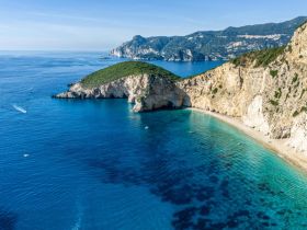 A stunning aerial view of a secluded beach and coastline, showcasing crystal-clear waters and lush greenery — an ideal destination for boat trips and exploration.