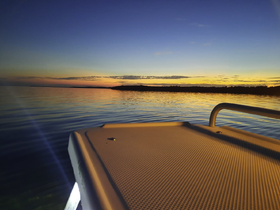 A serene sunset view from the deck of a boat, showcasing calm waters and a picturesque horizon — perfect for evening cruises.