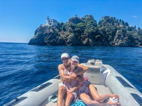 A happy couple enjoys a sunny day on a boat, with a stunning coastal landmark in the background — perfect for romantic getaways or scenic tours.