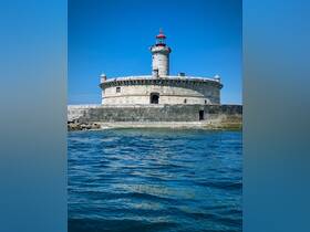 A scenic view of a lighthouse standing on a rocky shore, surrounded by clear blue waters, ideal for maritime photography.