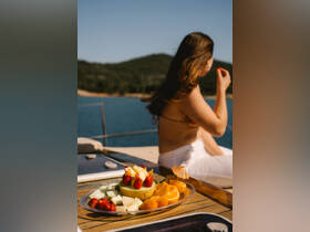 A beautifully arranged fruit platter sits on the deck of a boat, while a woman enjoys the view, perfect for a refreshing snack during a day on the water.