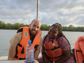 A cheerful couple wearing life jackets enjoys their time on a boat, surrounded by scenic waters and greenery — perfect for adventure seekers.